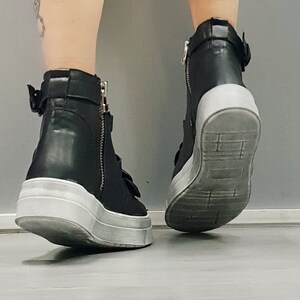 May include: Black leather high-top sneakers with white soles and buckle accents.