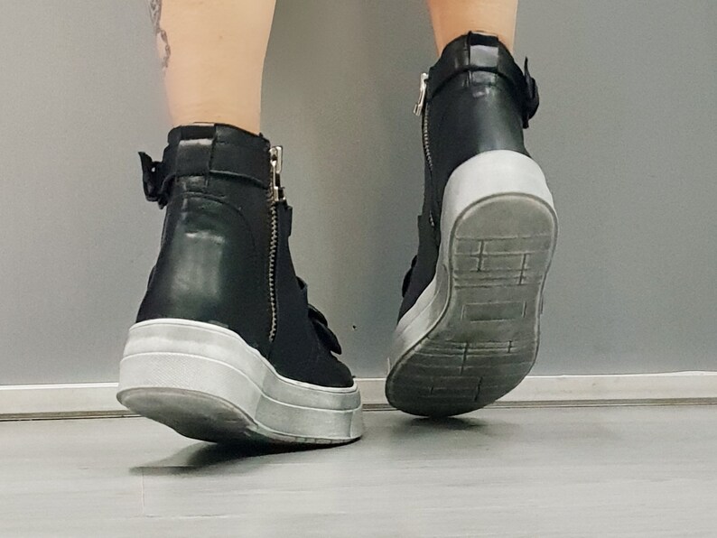 May include: Black leather high-top sneakers with white soles and buckle accents.