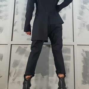 May include: A black blazer with a long, asymmetrical hemline, worn with black pants and black heeled boots with zipper accents.