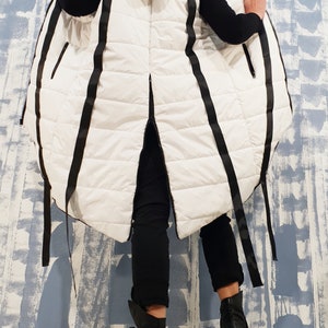 May include: A white puffer vest with black ribbon detailing. The vest has a hood and a long, flowing design.