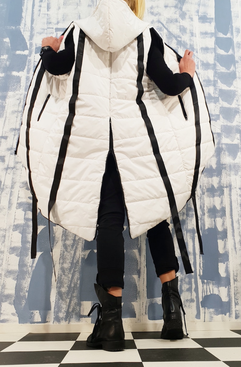 May include: A white puffer vest with black ribbon detailing. The vest has a hood and a long, flowing design.