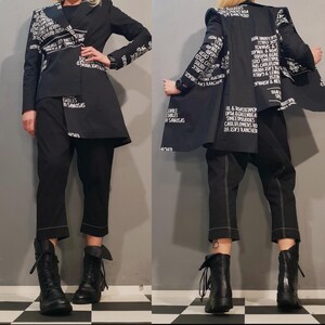 Peut inclure: Un blazer noir avec du texte blanc imprimé partout. Le blazer a une longue ligne d'ourlet asymétrique et est porté avec un pantalon noir et des bottes noires à lacets.