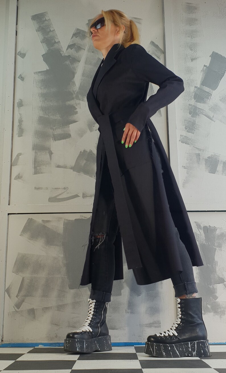 May include: A black long-sleeved coat with a belt and a long slit on each side. The coat is worn over black jeans and black and white platform boots.