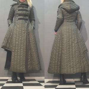 Può includere: Cappotto trapuntato verde oliva con gonna svasata e collo con cappuccio. Il cappotto presenta finiture nere e un design unico, offrendo un'opzione di capospalla elegante e calda. Lunghezza lunga, adatto al freddo.