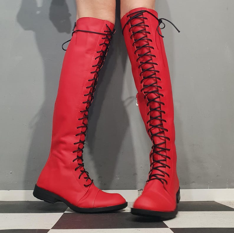 May include: A pair of vibrant red knee-high boots with black laces. The boots have a sleek design, featuring a lace-up closure that extends from the toe to the top of the boot. The boots are made of a smooth material and have a low heel.