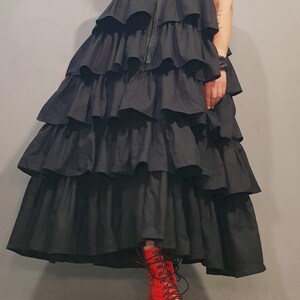 May include: A black sleeveless dress with multiple layers of ruffles. The dress has a zipper up the front and is worn with red lace-up boots.