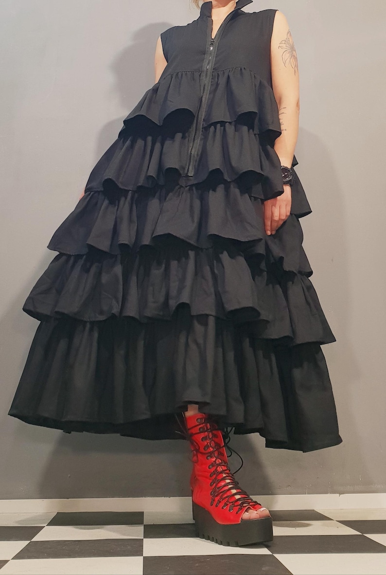 May include: A black sleeveless dress with multiple layers of ruffles. The dress has a zipper up the front and is worn with red lace-up boots.