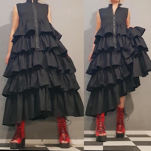 May include: A black tiered maxi dress with a zipper up the front and a ruffled hem. The dress is asymmetrical, with one side longer than the other. The model is wearing red platform boots.