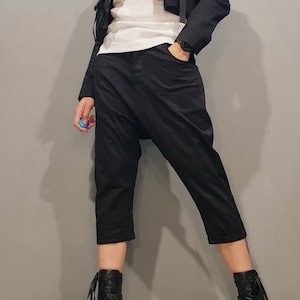 May include: A woman wearing a black cropped jacket with a white shirt and black pants. She is wearing black lace-up boots with a chunky heel.