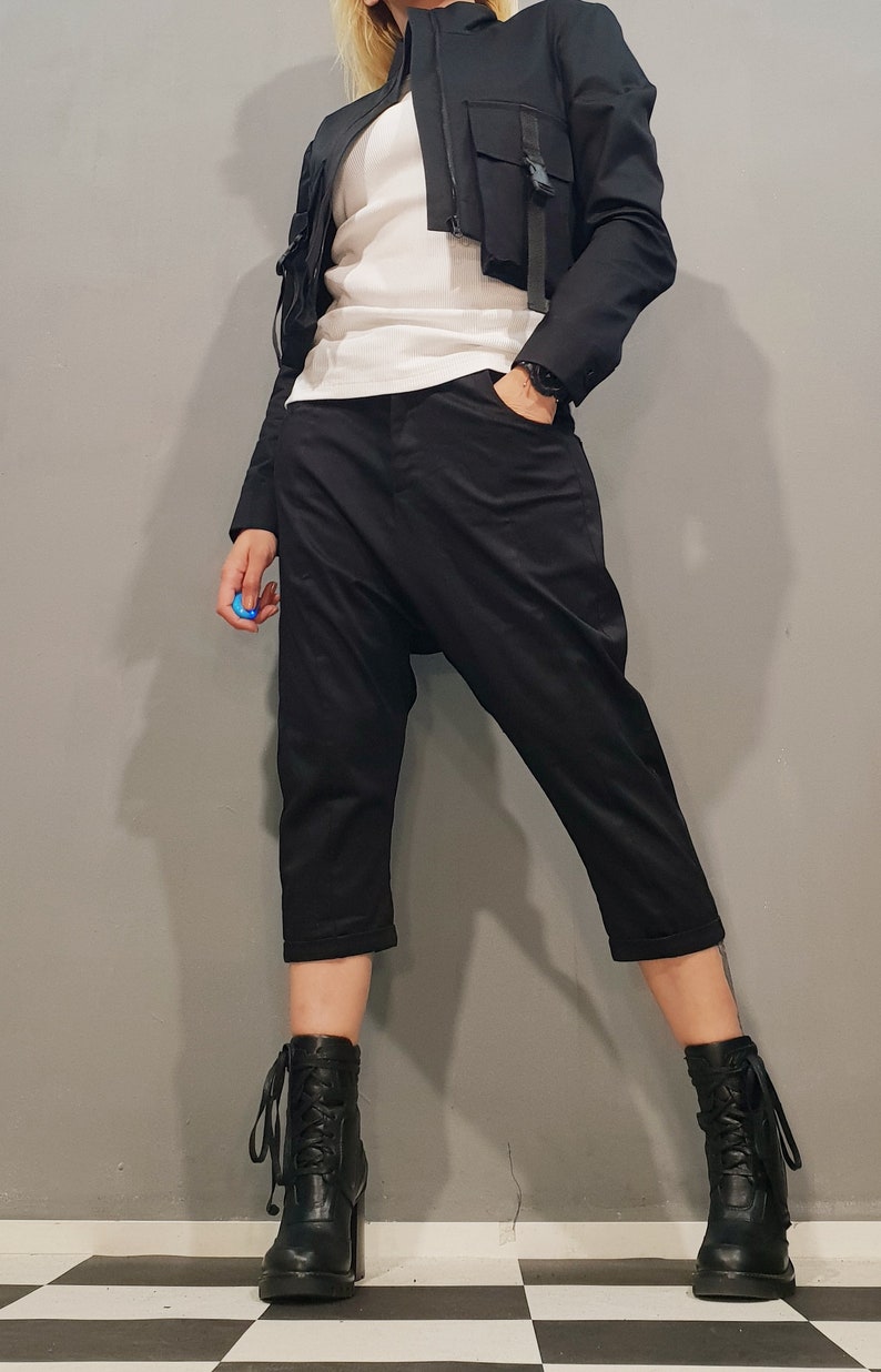 May include: A woman wearing a black cropped jacket with a white shirt and black pants. She is wearing black lace-up boots with a chunky heel.