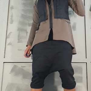 May include: A woman wearing a brown jacket with a black vest, black pants, and black boots. She is wearing sunglasses and has her hair pulled back in a ponytail.