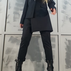 May include: A black blazer with a double-breasted closure and a long, asymmetrical hemline. The blazer is paired with black pants and black heeled boots with zippers.