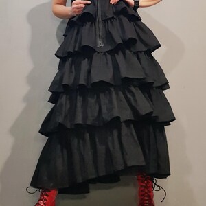 May include: A black sleeveless dress with a zipper down the front and multiple layers of ruffles. The dress is worn with red platform sandals.