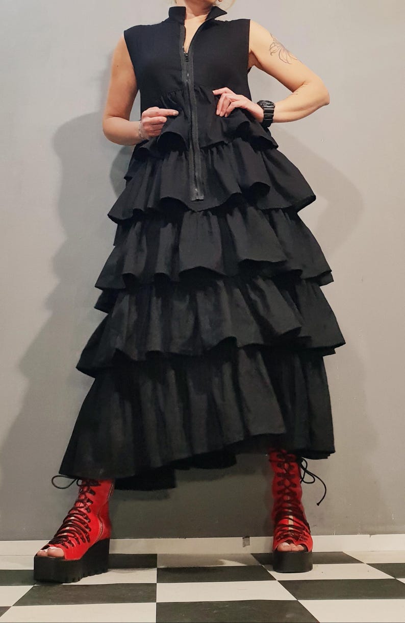 May include: A black sleeveless dress with a zipper down the front and multiple layers of ruffles. The dress is worn with red platform sandals.