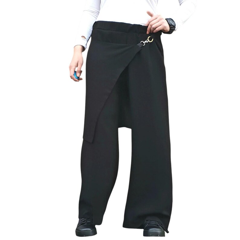 May include: Black wrap-style pants with a wide leg design. The pants feature a unique asymmetrical overlay secured with a gold-colored clasp. The fabric appears to be a smooth, solid black material, creating a sleek and modern look.