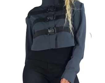 May include: A dark gray cropped jacket featuring a high collar and three horizontal black straps across the front, each secured with a black plastic side-release buckle. The jacket has long sleeves and a structured, fitted silhouette.