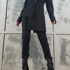 May include: A black blazer with a long, asymmetrical hemline, worn with black pants and black heeled boots with zippers.