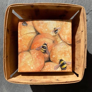 May include: A painting of a small canvas with a still life of oranges and bumblebees. The oranges are stacked on top of each other and the bumblebees are flying around them. The painting is in a wooden crate.