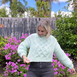 May include: A light green cable knit cropped sweater with a loose fit and long sleeves.