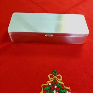 May include: A rectangular, brushed silver-tone metal storage box with a hinged lid and a small front latch. The container features a smooth, metallic finish and a clean, minimalist rectangular shape, providing a simple and functional design.