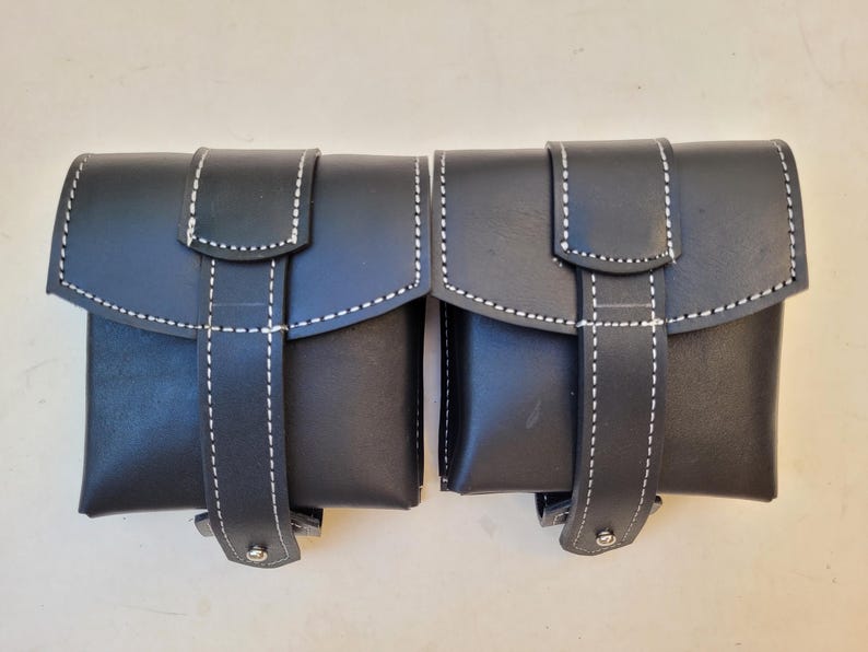 Pu&ograve; includere: Due borse in pelle nera con cuciture bianche e chiusura a fibbia. Le borse sono collegate tra loro.