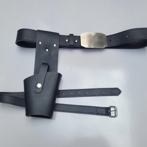 May include: A black leather belt with a silver buckle and a holster attached. The holster has a flap that can be secured with a snap.