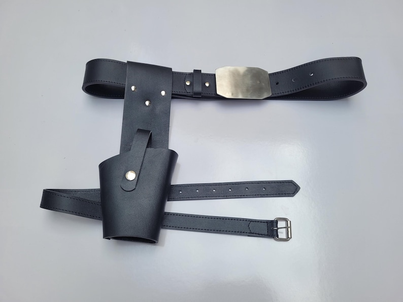 May include: A black leather belt with a silver buckle and a holster attached. The holster has a flap that can be secured with a snap.