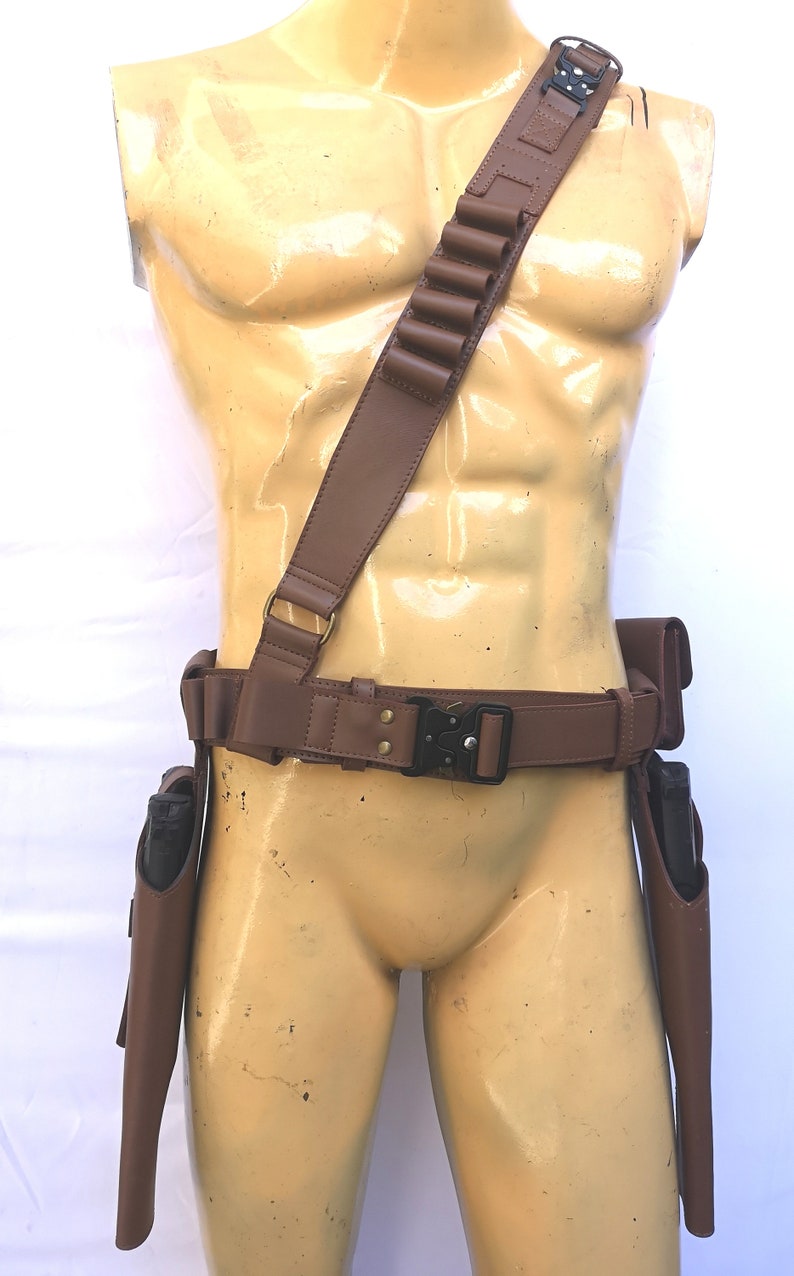 May include: A brown leather belt with a black buckle and a matching brown leather shoulder strap with loops for carrying ammunition. Two brown leather holsters are attached to the belt, each holding a black pistol.