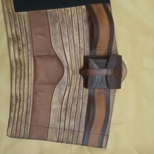 Może przedstawiać: Brązowy sk&oacute;rzany pasek z małą sk&oacute;rzaną saszetką. Pasek ma czarną gumową taśmę z tyłu i jest wykonany z kilku kawałk&oacute;w sk&oacute;ry zszytych ze sobą.