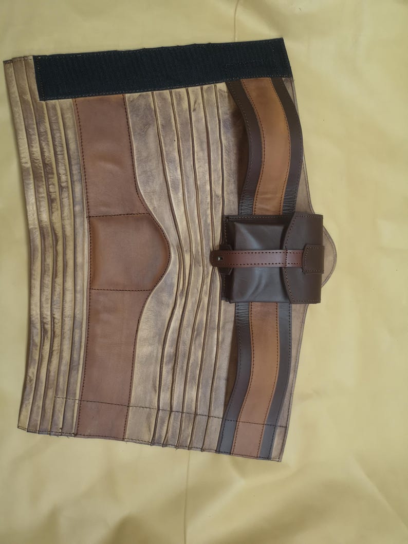 Może przedstawiać: Brązowy sk&oacute;rzany pasek z małą sk&oacute;rzaną saszetką. Pasek ma czarną gumową taśmę z tyłu i jest wykonany z kilku kawałk&oacute;w sk&oacute;ry zszytych ze sobą.