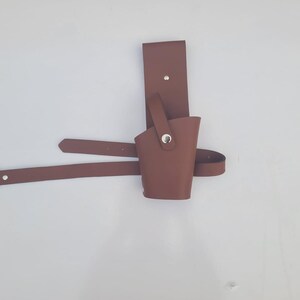 May include: A brown leather holster with a belt loop and a metal snap. The holster is designed to hold a small object, such as a knife or a tool.