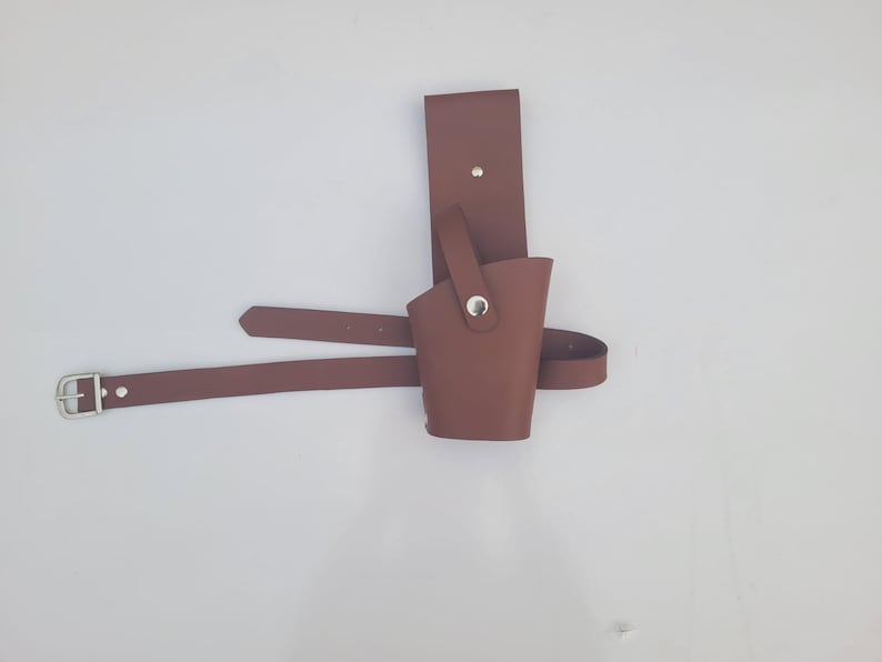 May include: A brown leather holster with a belt loop and a metal snap. The holster is designed to hold a small object, such as a knife or a tool.