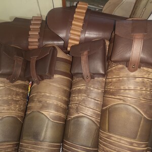 Może przedstawiać: Cztery brązowe sk&oacute;rzane sakiewki z paskami i klamrami. Sakiewki są przymocowane do szerszego brązowego sk&oacute;rzanego pasa z rzędem metalowych ćwiek&oacute;w.