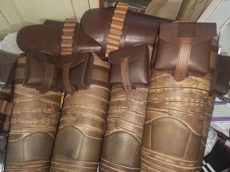 Może przedstawiać: Cztery brązowe sk&oacute;rzane sakiewki z paskami i klamrami. Sakiewki są przymocowane do szerszego brązowego sk&oacute;rzanego pasa z rzędem metalowych ćwiek&oacute;w.