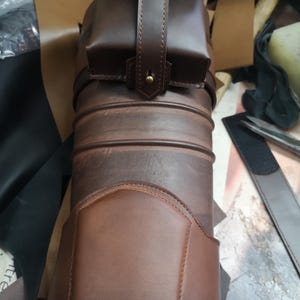 Może przedstawiać: Brązowy sk&oacute;rzany kołczan z małą kieszenią przymocowaną do g&oacute;ry. Kołczan ma ozdobne przeszycia i jest wykonany z wysokiej jakości sk&oacute;ry.