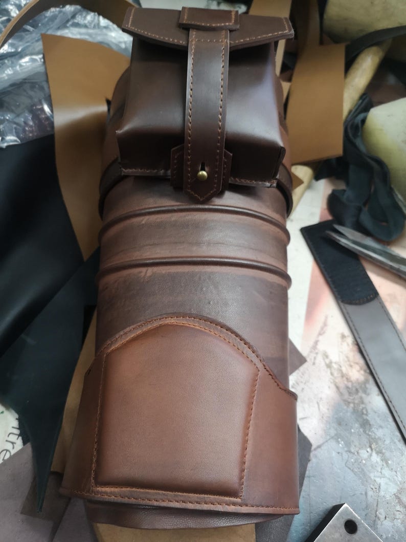 Może przedstawiać: Brązowy sk&oacute;rzany kołczan z małą kieszenią przymocowaną do g&oacute;ry. Kołczan ma ozdobne przeszycia i jest wykonany z wysokiej jakości sk&oacute;ry.