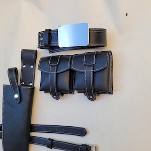 Pu&ograve; includere: Una cintura in pelle nera con una fibbia argentata e due sacche in pelle nera con cuciture bianche. Le sacche hanno una patta con chiusura a fibbia. La cintura &egrave; fissata a un fodero in pelle nera con un bottone argentato.