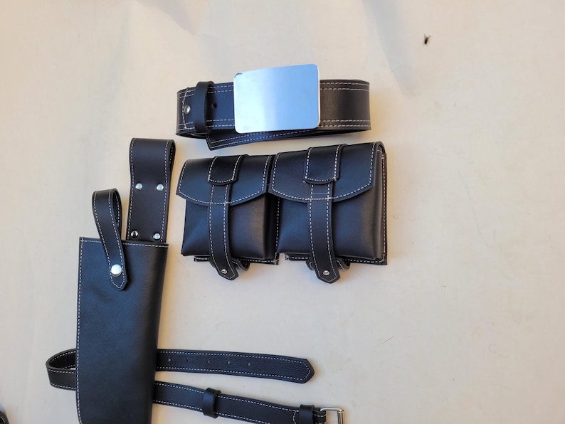 Pu&ograve; includere: Una cintura in pelle nera con una fibbia argentata e due sacche in pelle nera con cuciture bianche. Le sacche hanno una patta con chiusura a fibbia. La cintura &egrave; fissata a un fodero in pelle nera con un bottone argentato.