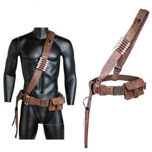 May include: A brown leather belt with a holster and a shoulder strap. The belt has a metal buckle and a pouch on the right side. The shoulder strap has a pouch on the left side and a row of silver bullet casings.