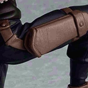 Puede incluir: Una figura negra y marrón con una rodillera de cuero marrón. La figura lleva pantalones negros y una camisa roja.