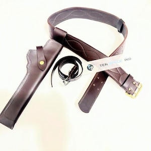 May include: A dark brown leather gun holster, belt, and a smaller belt with a silver buckle. The larger belt has a gold buckle and decorative stitching. The text "TEN STYLE IND" is visible on a tag.