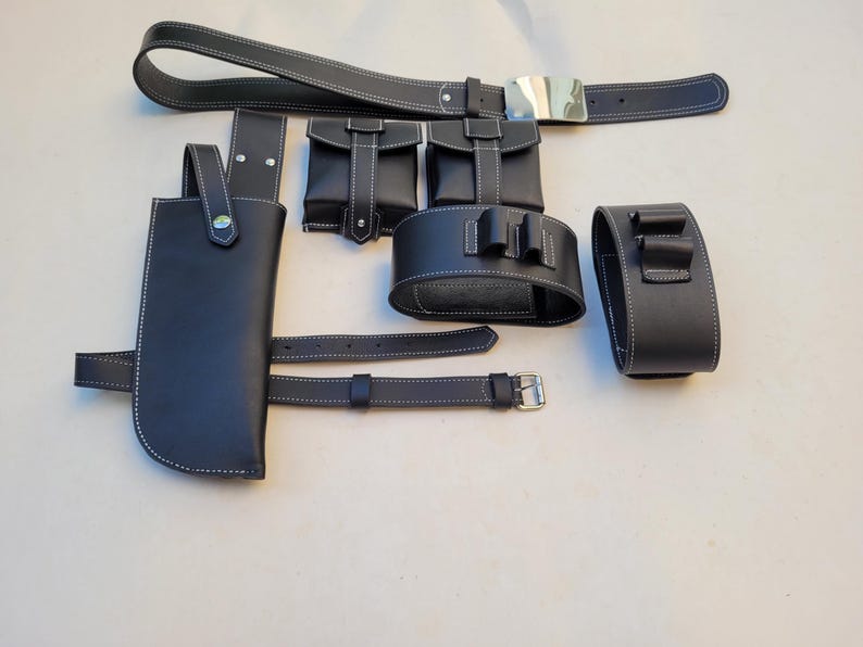 Pu&ograve; includere: Una cintura in pelle nera con fibbia argentata e pi&ugrave; tasche e cinturini. La cintura &egrave; decorata con cuciture bianche.