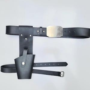 May include: Black leather belt with a silver buckle and a holster attached. The holster has a flap that can be secured with a snap.