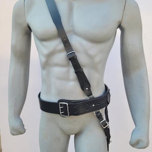May include: A black leather belt with a silver buckle and a matching shoulder strap. The belt has a series of small holes for adjusting the fit.
