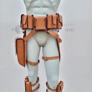 Pode incluir: Um cinto de couro castanho com múltiplos bolsos e correias. O cinto tem uma fivela e é usado em um manequim. O cinto tem correias para a coxa e correias para as pernas com bolsos.