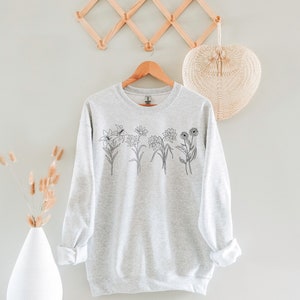 Pode incluir: Uma camisa de moletom cinza com um desenho de linha preta de uma variedade de flores na frente.