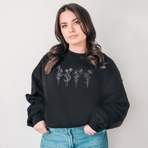 Pode incluir: Uma camisa de moletom preta com um contorno branco de uma fileira de flores na frente.