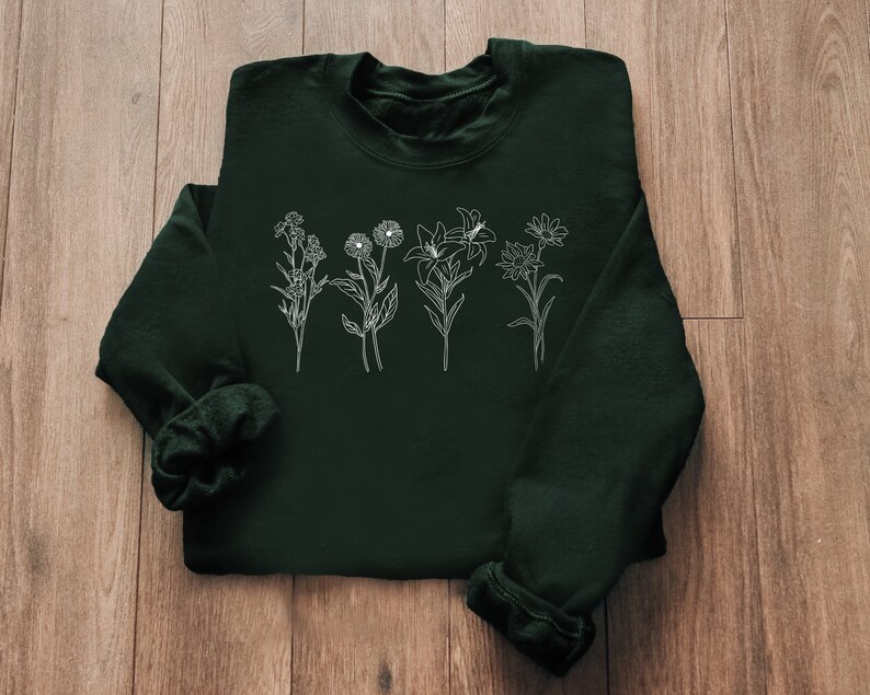 Pode incluir: Uma camisa de moletom verde escura com um contorno branco de v&aacute;rias flores na frente.