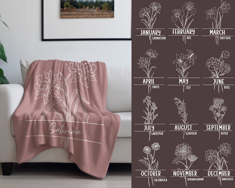 May include: A dusty rose throw blanket with a white floral design and the name "Sabrina" in a white rectangular box. The blanket is draped over a white sofa. A chart of birth month flowers is on the right.