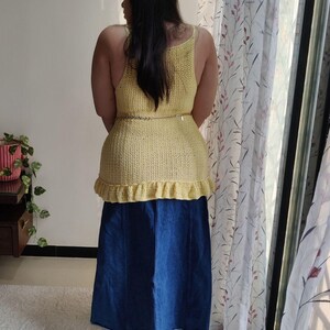 Puede incluir: Un top de crochet amarillo con un dobladillo con volantes y un fino cintur&oacute;n de cadena dorada. El top se lleva sobre una falda vaquera azul.
